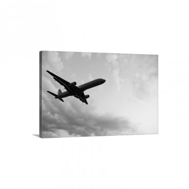 A Silhouetted Airplane Flies Among A Few Clouds Wall Art - Canvas - Gallery Wrap