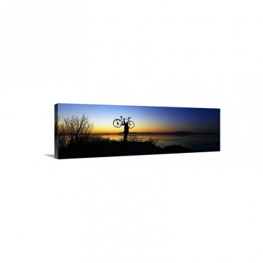Silhouetted Cyclist Holding Bicycle Over Head River's Edge Sunset Alaska Wall Art - Canvas - Gallery Wrap